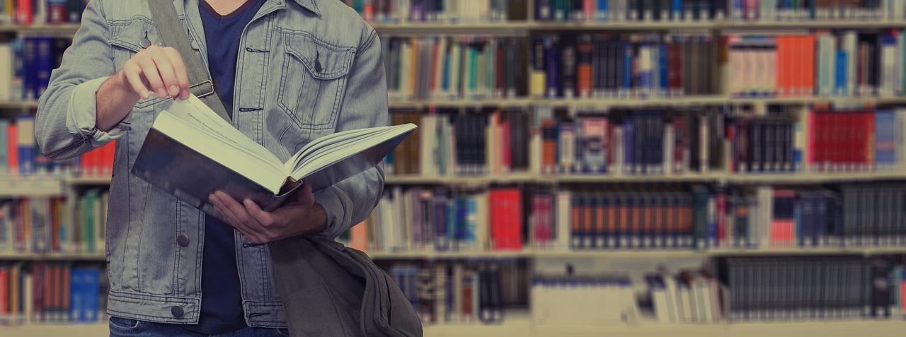 A male student standing in a library reading a book
